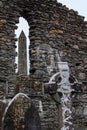 The Round Tower viewed through a window in a stone wall with a Celtic cross and grave stones in the foreground at the Glendalough Royalty Free Stock Photo