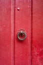 A round and twisted cast iron door knocker fitted on an old wooden door painted in red Royalty Free Stock Photo