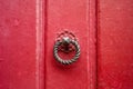 A round and twisted cast iron door knocker fitted on an old wooden door painted in red