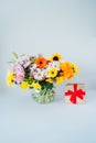 Round Vase with huge multicolor various mixed flower bouquet and shining golden gift box with red velvet ribbon on