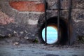Round water drain window in red brick wall behind metal bars with view on blue sea water Royalty Free Stock Photo