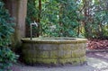 Round water well with faucet in a cemetery with old trees