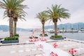 Round wedding arch stands on a pier with moored yachts in front of rows of white chairs