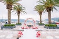 Round wedding arch stands on a pier with palm trees in front of rows of white chairs Royalty Free Stock Photo