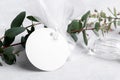 Round white gift tag mockup with eucalyptus leaves on grey background, label tag mockup, Wedding favor tag