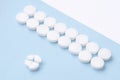 Round white medical pills arranged and one of them is crushed into four parts on blue background. Pill splitting Royalty Free Stock Photo