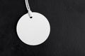 Round white tag mockup with white cord, close up. Blank paper price tag isolated on black background