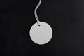 Round white tag mockup with white cord, close up. Blank paper price tag isolated on black background