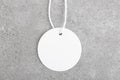 Round white tag mockup with white cord, close up. Blank paper price tag isolated on grey stone background