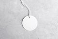 Round white tag mockup with white cord, close up. Blank paper price tag isolated on grey stone background