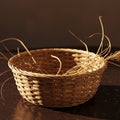 A round wicker basket sits on a dark surface, partially filled with dry straw or grass. Th Royalty Free Stock Photo