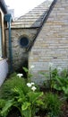 Round window, beige slate stacked stone wall and white calla lilies. Royalty Free Stock Photo