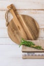 Round wood cutting board, stack of linen towels, rosemary twig tied with twine on white plank wood background Royalty Free Stock Photo