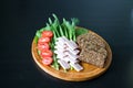 On a round wooden Board is sliced black bread with seeds, smoked brisket, green onions, lettuce, tomatoes and dill. Black Royalty Free Stock Photo