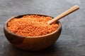 A round wooden bowl filled with red lentils with a wooden spoon stands on a dark background