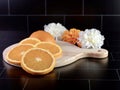 Round wooden cutting board with a handle with a fresh orange sliced up and arranged on it with 3 artificial white and orange Royalty Free Stock Photo