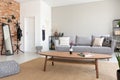 Round wooden table in the middle of elegant living room with grey sofa, metal shelf and mirror, real photo with copy space