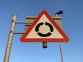 Roundabout ahead warning sign against a clear blue sky