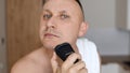 Daily routine male self-care. Handsome young unshaven man with towel on shoulders shaving with modern electric razor Royalty Free Stock Photo