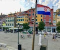 A view of the waterfront in the old town of Rovinj, Croatia. People are walking along the boardwalk with the croatian flag flying