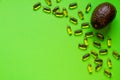 Row avocado on green backgroundand lots of capsules with avocado oil or fish oil, creative food concept Royalty Free Stock Photo