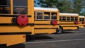 Row of back ends of parked yellow school buses with red safety stop signs used to signal oncoming traffic when loading and