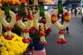 Row of beautiful fresh elaborated flower garlands in Thai style hanging on pandan leaves with local morning market background