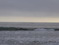 Row boats in the pacific in Santa Monica, cloudy sky after sunset, a sailboat to the right, one little wave in the foreground Royalty Free Stock Photo