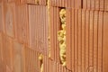 Row of bricks in red and orange color with the inner gap filled with isolating foam on the construction site