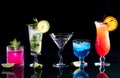 A row of bright colourful cocktails on a glass table, against black.