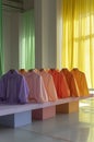 A row of brightly colored shirts arranged on pastel blocks.