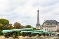 The row of bronze cannon of the Place des Invalides in Paris, France, and the Eiffel tower under a cloudy sky