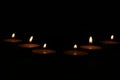 A row of burning tealight candles in a darkened room