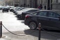 A row of cars parked in a Parking lot against the background of a street and pedestrians with a black car in the