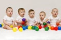 Row of caucasian babies sitting side by side looking away isolated on gray background. Five cute babies playing with Royalty Free Stock Photo