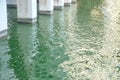 A row of cement pillars of a high building in green lake water with waves