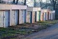 Concrete garages with colorful metal doors in morning sunlight along a road through alley of trees