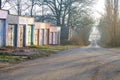 Concrete garages with colorful metal doors in morning sunlight along a road through alley of trees