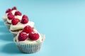 A row of cupcakes with white cream and raspberries on a blue background sharpness in the foreground.