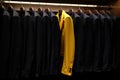 A row of dark suits with one bright yellow suit. Ai generated. Royalty Free Stock Photo