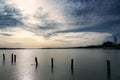 Row of dark wooden piles on a frozen lake under a sky with interesting clouds, in late winter the earth stands still while there