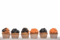 Row of delicious Halloween orange and black cupcakes isolated on white.