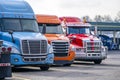 Row of different big rigs semi trucks on truck stop parking lot waiting for continuation of the road routes