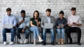 Row of diverse young people sitting by wall using gadgets