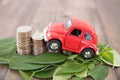 A row of dollar coins surrounded by fresh green leaves and cars climbing on them