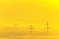 Row of electricity poles lines on field in morning fog during sunrise in the morning. Royalty Free Stock Photo