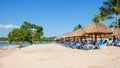 Row of empty lounger chairs under beach sun umbrellas made from palm tree leaves on the atlantic ocean coastline