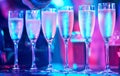 A row of full champagne glasses illuminated with pink and blue lights