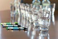 a row of glasses of water in front of a row of pens on a conference table