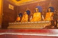 Row of golden Buddha images in temple at Shwedagon Pagoda and monk deep in devotion on step below